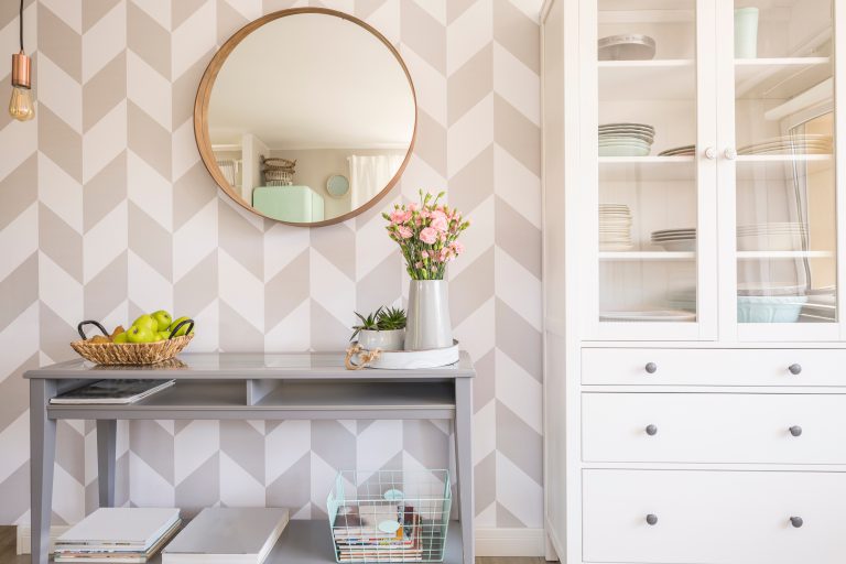Mirror on patterned wallpaper above grey table with flowers in scandi living room interior. Real photo